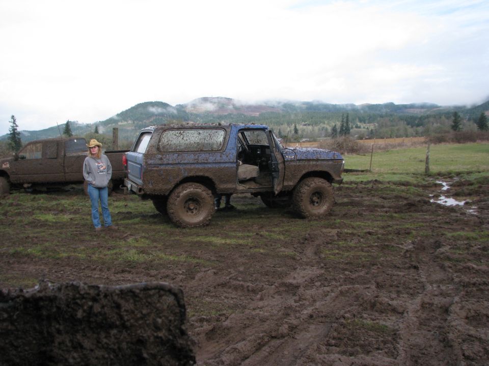 Mud-covered blue 1978 Ford Bronco parked in a muddy field with a person standing nearby