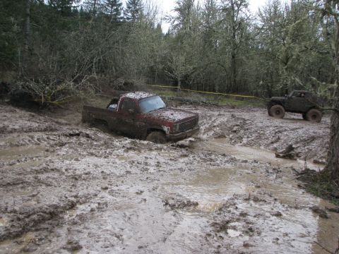 1978 Ford Bronco - Two off-road vehicles navigate a muddy terrain, with one truck deeply stuck in the mire.