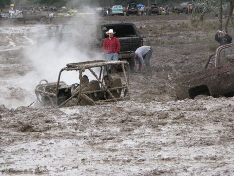 1978 Ford Bronco - Multiple vehicles are stuck in deep mud during an off-road event, with spectators observing the scene.
