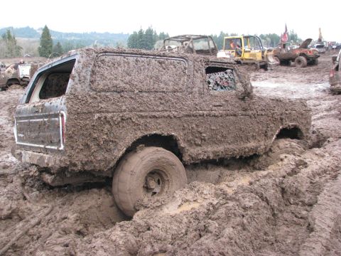 1978 Ford Bronco - A heavily mud-caked 1978 Ford Bronco is stuck in a muddy terrain with other vehicles visible in the background.