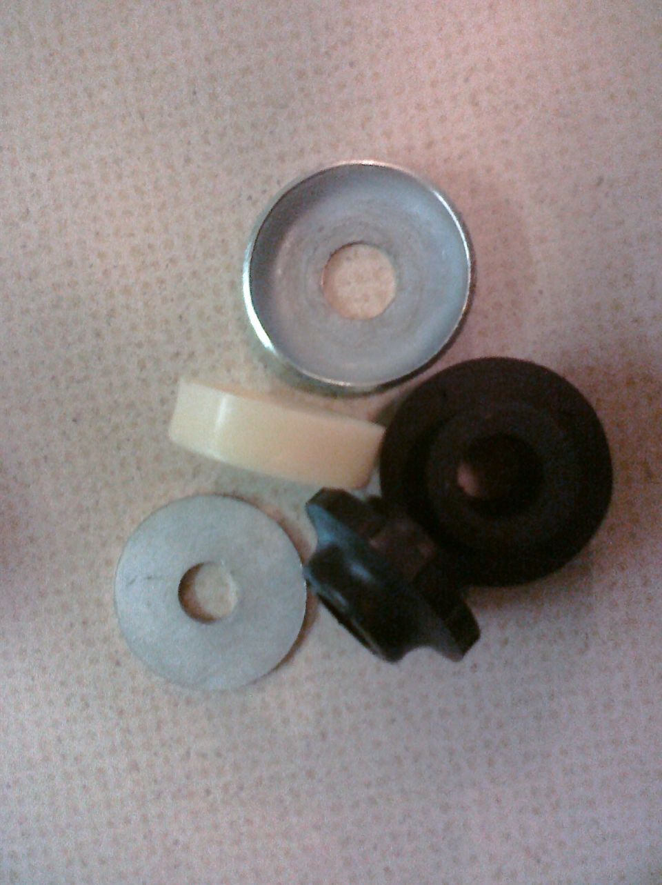 Several washers, a rubber grommet, and a plastic bushing are laid out on a textured surface