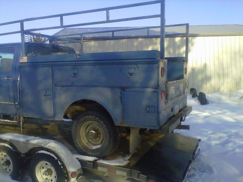 1994 Ford F-150 - A blue pickup truck with a utility bed and rack is loaded onto a trailer in a snowy environment.