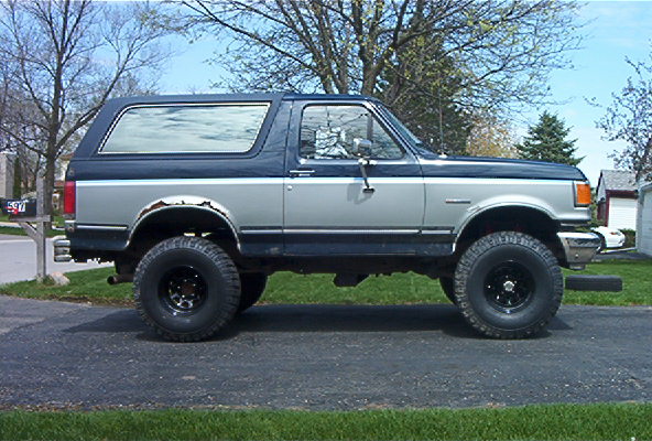 Side view of a lifted Ford Bronco with aftermarket wheels and tires. The vehicle has a two-tone paint scheme