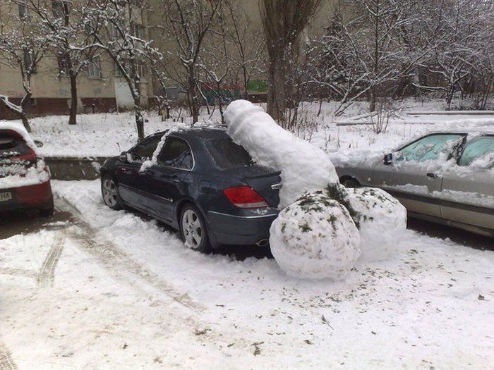 Dark sedan in snowy lot with large rolled snowballs beside it