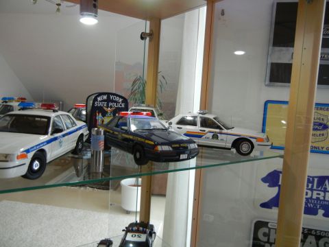 1999 Lincoln Town Car - A collection of police car models, New York State Police vehicles, are showcased on shelves in a display case.