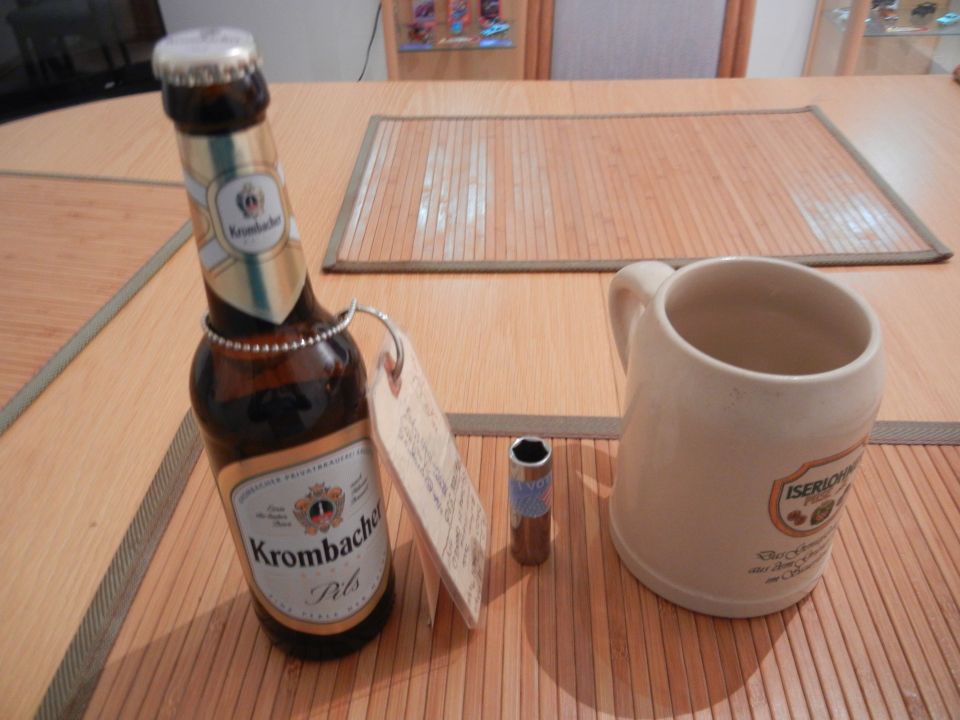 Krombacher Pils bottle, ceramic mug, and a single socket wrench bit on a wooden table