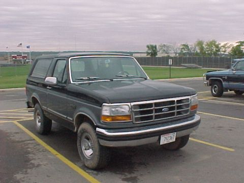 1993 Ford Bronco - A dark green and black Ford Bronco is parked in a lot, with another vehicle visible in the background.
