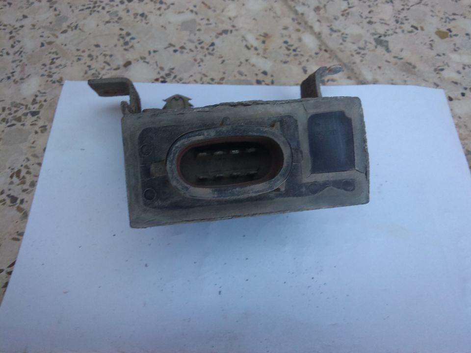 Close-up of a dusty, rectangular automotive electrical connector with a large oval socket and metal mounting tabs
