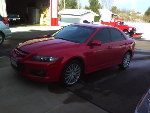2006 Mazda 6 - A red 2006 Mazda 6 sedan is parked outside a garage with a red truck in the background.