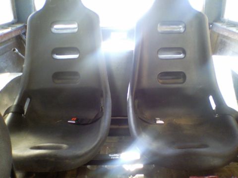 1989 Ford Bronco - The interior of a vehicle shows two black bucket seats with visible seatbelts and harness slots.