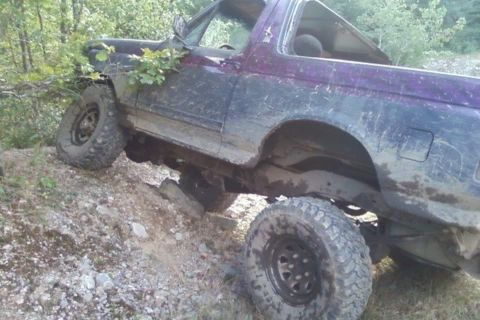 1989 Ford Bronco - This off-road vehicle is navigating a steep, rocky incline in a wooded area.