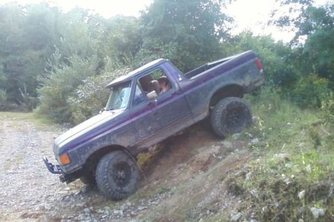 1989 Ford Bronco - Purple Ford Bronco navigates an off-road incline with its front-left tire lifted.