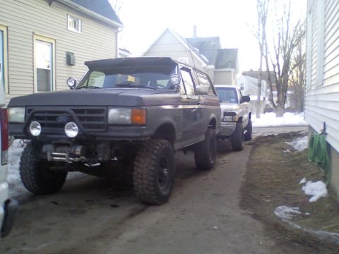 1989 Ford Bronco - This modified SUV, likely a 1987 Ford Bronco, is parked in a driveway with a pickup truck behind it.