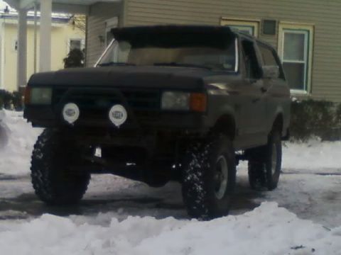 1989 Ford Bronco - This modified Ford Bronco is equipped with large off-road tires and auxiliary lights, seen in a snowy environment.
