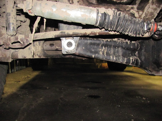 Underside suspension parts with dirt and grime. A metal bracket is bolted to a black arm