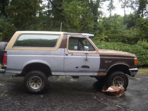 1989 Ford Bronco - A side view of a Ford Bronco with visible body damage and mismatched paint sections.