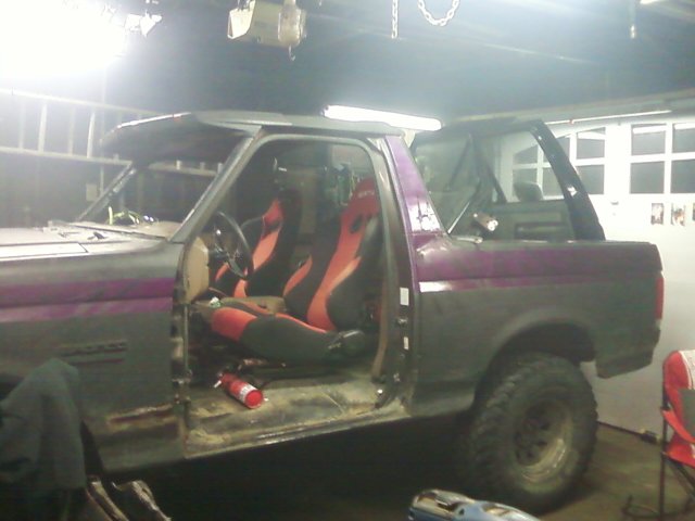 Ford Bronco with racing seats and a fire extinguisher, viewed from the side in a garage