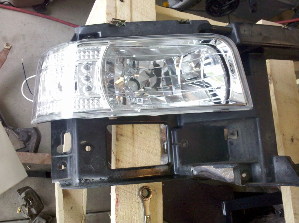 Aftermarket clear crystal headlight assembly resting on a black headlight mounting panel
