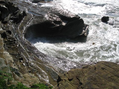 1971 Ford Ranchero - Waves crash against the dark, wet rocks of a coastline, with sunlight glinting off the water.