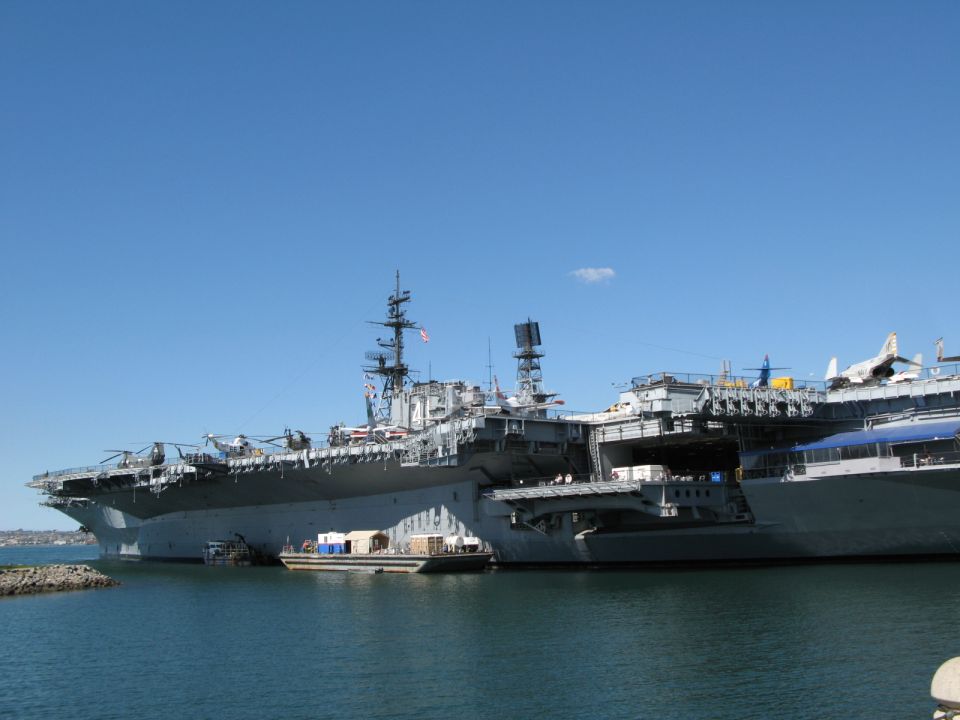 Grey aircraft carrier museum ship moored at a pier with aircraft on the flight deck