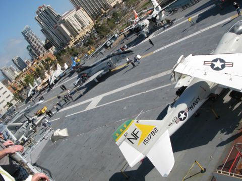 1971 Ford Ranchero - An aircraft carrier deck is filled with various fighter jets, with a city skyline in the background. Several Navy aircraft are on display.