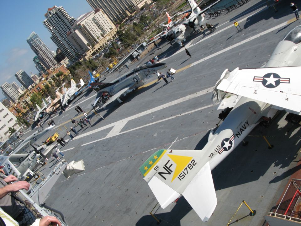 Navy museum carrier flight deck with parked jets and a city skyline behind
