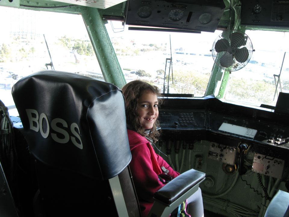 Child seated beside a black 'BOSS' captain's chair in a green ship's bridge