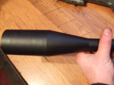 1996 Ford Bronco - A hand holds a black rifle scope, which is resting on a wooden table.