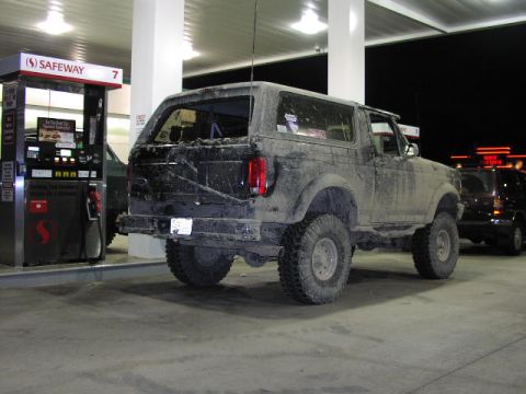 1981 Ford Bronco - This heavily muddied Ford Bronco is parked at a gas station, with another vehicle visible behind it.