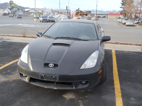 2006 Ford E350 - A dark gray Toyota Celica is parked in a lot, showing its front end with a distinctive hood scoop.