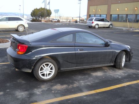 2006 Ford E350 - Passenger-side rear three-quarter view of a black Toyota Celica liftback coupe with rear wing, whip antenna and silver five-spoke alloys, i…