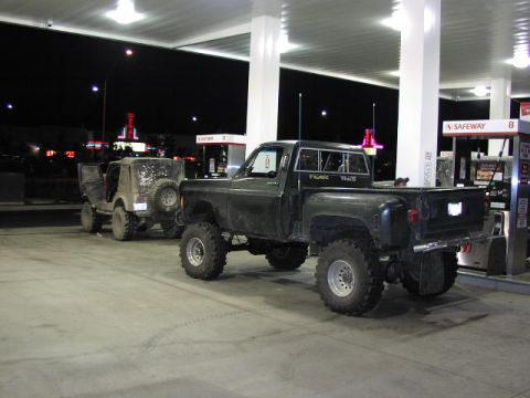 1981 Ford Bronco - Two , lifted off-road vehicles are parked at a gas station under the bright lights at night.