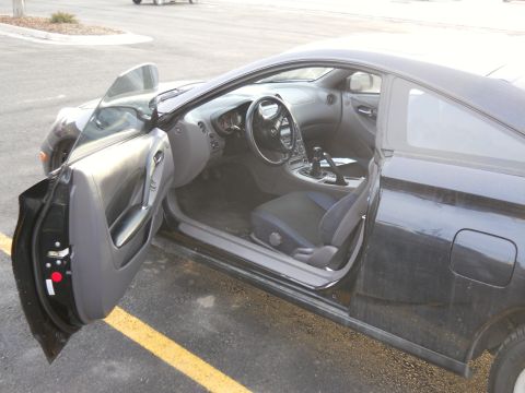2006 Ford E350 - Driver's door open on a black Toyota Celica coupe, showing the gray door card, gray-and-black cloth bucket seat, three-spoke steering wheel…