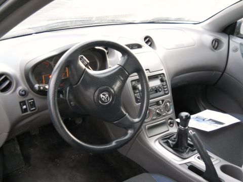 2006 Ford E350 - Driver's side interior of a Toyota Celica shot from the passenger seat, showing the three-spoke leather steering wheel with Toyota badge, o…
