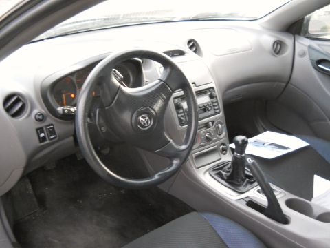 2006 Ford E350 - Driver's-side dashboard of a Toyota Celica in gray plastic, showing the three-spoke leather steering wheel with Toyota badge, hooded gauge…