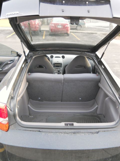 2006 Ford E350 - Open rear hatch of a silver Toyota liftback coupe showing the empty carpeted cargo area, folded rear seatbacks and gray cloth front bucket…