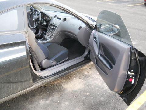 2006 Ford E350 - Passenger door open on a black Toyota Celica coupe, showing the gray and black cloth bucket seats, gray dash with center-stack radio, three…