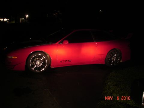1997 Ford Probe - A red sports car with aftermarket wheels is parked outdoors at night, illuminated by artificial light.