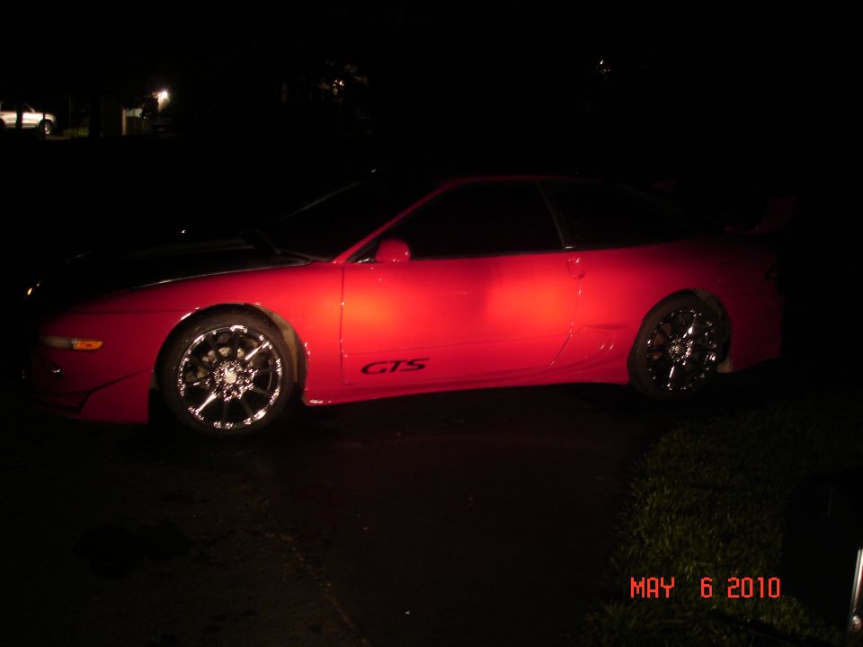 Red sports car with chrome wheels and a 'GTS' decal on the side, viewed from the side at night