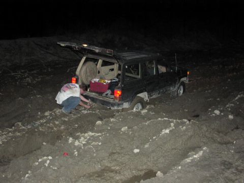 1981 Ford Bronco - A person is attempting to free a Jeep Cherokee that is stuck in thick mud at night.