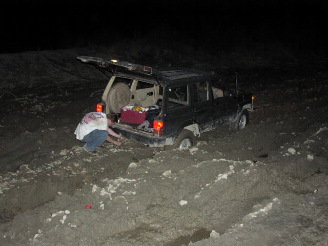 Person hooking up a tow strap to a Jeep Cherokee stuck in mud at night