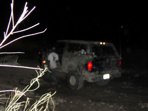 1981 Ford Bronco - A muddy SUV is seen from the rear at night, with its taillights illuminated.