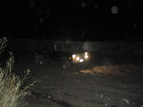 1981 Ford Bronco - A black pickup truck navigates a muddy terrain at night, its headlights illuminating the path ahead.
