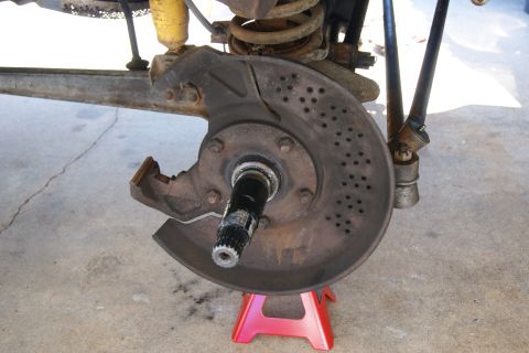 1978 Ford Bronco - Close-up of a vehicle's brake rotor and suspension components, supported by a red jack stand.