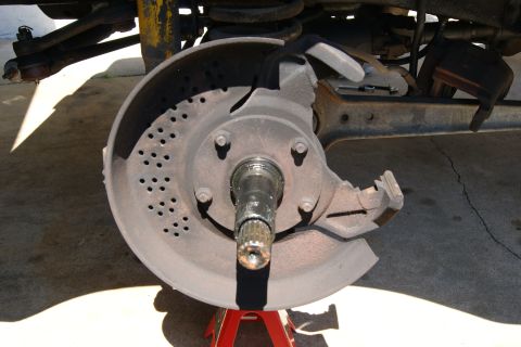 1978 Ford Bronco - Close-up view of a vehicle's front brake rotor and suspension components, supported by red jack stands.