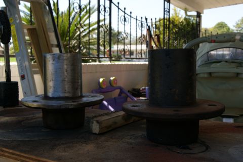 1978 Ford Bronco - Two vehicle wheel hubs are displayed on a workbench outdoors, with a fence and greenery in the background.