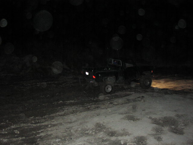 Pickup truck with headlights on, driving on a snowy or muddy path at night
