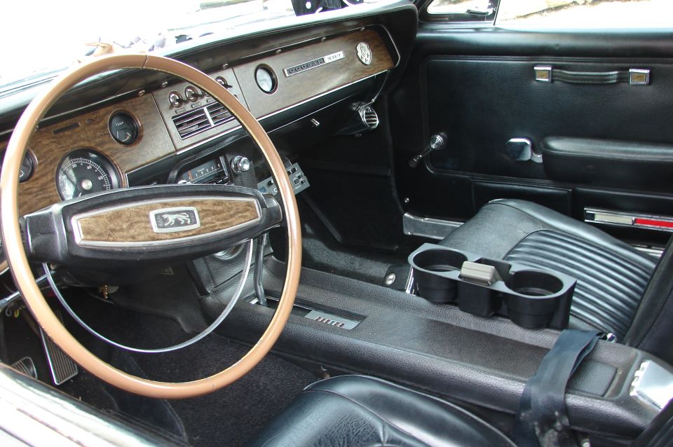 1968 Mercury Cougar interior with wood grain dash, steering wheel, and black seats. Center console has cup holders