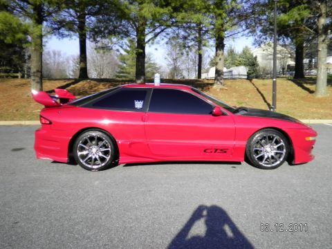 1997 Ford Probe - A red sports coupe is shown from the side, a prominent rear spoiler and custom wheels. The 'GTS' decal is visible on the lower body.