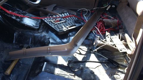 1994 Ford Bronco - Gutted truck interior with the carpet and seats removed, showing bare painted floor pan, seat mounting studs and drain plugs. A tan plastic…